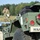 A military vehicle or trailer is shown in the foreground with the marking 'RES/2CAV' and unit number '1042' stenciled on its olive-drab green body. A soldier in camouflage uniform holding a clipboard or document is visible in the blurred background. The setting appears to be an outdoor military training or operational area with a treeline in the background.