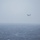 Marine F-35B Lightning II fighter aircraft complete GAU-22 cannon, ordnance hot reload exercise in Indo-Pacific Region A tiltrotor aircraft, consistent with a V-22 Osprey, is flying over a rough, open ocean under overcast and hazy conditions. A bright red spherical object, likely a buoy or marker, is visible floating on the water's surface below and to the left of the aircraft. The scene suggests a maritime search, rescue, or recovery operation.