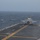 Marine F-35B Lightning II fighter aircraft complete GAU-22 cannon, ordnance hot reload exercise in Indo-Pacific Region A military jet aircraft, consistent with an F-35B, is positioned on the flight deck of an amphibious assault ship or aircraft carrier at sea. The aircraft appears to be preparing for takeoff or has just landed, facing toward the bow of the ship. Sea conditions appear rough with whitecaps visible, and the sky is overcast.