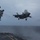 Marine F-35B Lightning II fighter aircraft complete GAU-22 cannon, ordnance hot reload exercise in Indo-Pacific Region An F-35B Lightning II stealth fighter jet is captured in a short takeoff or vertical landing (STOVL) maneuver from the deck of an amphibious assault ship at sea. The aircraft's landing gear is deployed and a lift fan door is open on top of the fuselage, consistent with STOVL operations. The scene takes place under overcast, stormy conditions over open ocean.