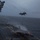 Marine F-35B Lightning II fighter aircraft complete GAU-22 cannon, ordnance hot reload exercise in Indo-Pacific Region Two F-35B Lightning II stealth fighter jets are visible on what appears to be an amphibious assault ship flight deck during adverse weather conditions. One aircraft is airborne in a short takeoff or vertical landing (STOVL) configuration, while a second sits on the deck below. The scene depicts active flight operations at sea under overcast, stormy skies with rough ocean conditions.
