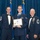 Airman Leadership School distinguished graduate Three U.S. Air Force personnel in dress uniforms pose for a formal photo at what appears to be a graduation or awards ceremony. The central figure, a younger airman, holds a framed diploma from the United States Air Force Airman Leadership School made out to 'SrA Jacob D. Lewandowski'. The two flanking individuals appear to be senior non-commissioned officers based on their rank insignia and medal arrays.