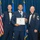 Airman Leadership School distinguished graduate Three U.S. Air Force personnel pose for a formal photograph at what appears to be an Airman Leadership School graduation ceremony. The central figure holds a framed diploma from the United States Air Force Airman Leadership School and wears a medallion/medal around his neck. The two flanking individuals wear dress blue uniforms with bow ties and display senior NCO rank insignia.