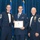 Airman Leadership School distinguished graduate Three U.S. Air Force personnel in dress uniforms are posed at what appears to be a formal military graduation or awards ceremony. The center individual is holding a framed diploma/certificate and wearing a medal on a blue ribbon around his neck. Two senior non-commissioned officers flank him, both wearing multiple service medals and ribbons.