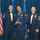 Airman Leadership School leadership award Three U.S. Air Force personnel in dress blue mess uniforms are posed together at a formal military awards ceremony. The central figure is holding a clear glass/acrylic award trophy, suggesting he is the recipient of a commendation or recognition. The two flanking individuals appear to be senior non-commissioned officers based on their rank insignia.
