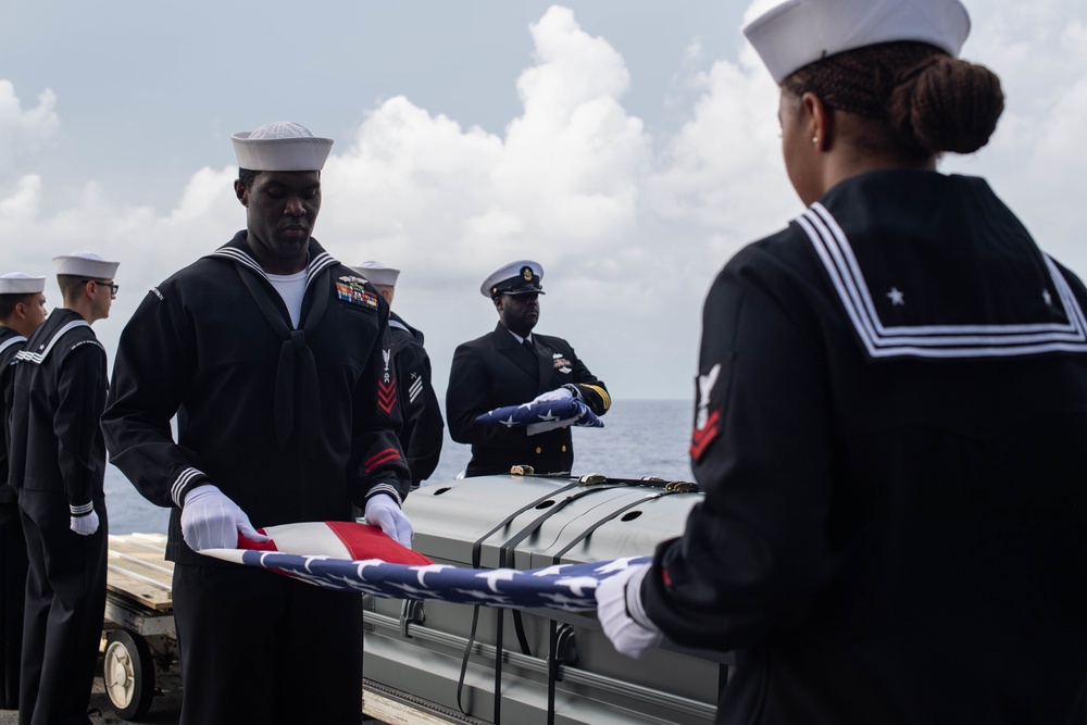 U.S. Sailors fold an America flag during a burial at sea