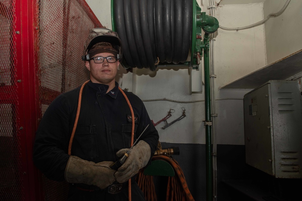 U.S. Navy Electrician’s Mate 3rd Class Michael Muller, from Reno, Nevada, poses at a fire station in the hangar bay of the aircraft carrier USS John C. Stennis (CVN 74)