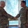 Two military personnel in OCP (Operational Camouflage Pattern) uniforms are shaking hands in what appears to be an indoor military facility. The individual on the right has visible 'U.S. AIR FORCE' tape and a 'CAP' (Civil Air Patrol) patch on their uniform. The setting suggests a formal recognition or greeting ceremony.