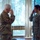 Two U.S. military personnel are exchanging salutes indoors, facing each other. The individual on the left wears an Army Combat Uniform (OCP/Multicam) with a U.S. flag patch, while the individual on the right wears a U.S. Air Force Airman Battle Uniform (ABU) with 'U.S. AIR FORCE' visible on the chest. The Air Force member is smiling, suggesting a positive or ceremonial interaction.