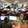 This image shows a busy FEMA (Federal Emergency Management Agency) operations center with numerous workstations arranged in rows. Staff members are actively working at computer terminals, coordinating emergency management activities. The facility displays FEMA branding and Department of Homeland Security signage, indicating this is an official federal emergency coordination hub.