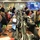 This image shows a busy FEMA (Federal Emergency Management Agency) operations center during what appears to be an active emergency response. Multiple personnel are working at workstations equipped with laptops and desktop monitors, while large display screens on the back wall show statistics and weather/geographic data. The room is densely populated with staff in both civilian and uniform attire, suggesting a coordinated multi-agency response effort.