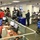 The image shows a busy emergency operations center (EOC) with numerous personnel working at computer workstations. A sign reading 'Situational Awareness Section' is prominently displayed, indicating this is an active emergency management facility. Multiple screens, monitors, and large display boards are visible throughout the room, suggesting real-time data monitoring and coordination activities.