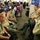 The image shows personnel gathered at FEMA's National Response Coordination Center, with four U.S. Forest Service employees in uniform having a discussion in the foreground. The busy operations center is filled with workstations, computers, and numerous staff members coordinating emergency response activities. The FEMA logo and signage are prominently displayed on the wall in the background.