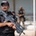 Anbar SWAT VIP training A SWAT officer in the foreground holds a compact assault rifle while wearing tactical gear including a black vest and SWAT-labeled cap. Multiple additional personnel in tactical uniforms are visible in the blurred background. The scene appears to be a security deployment or demonstration.
