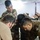 Anbar SWAT VIP training Several military personnel in camouflage uniforms are gathered around a table, examining printed aerial or satellite imagery documents. One individual in civilian clothing is also participating in the briefing or planning session. A soldier is using a smartphone to reference additional information while pointing at the printed materials.