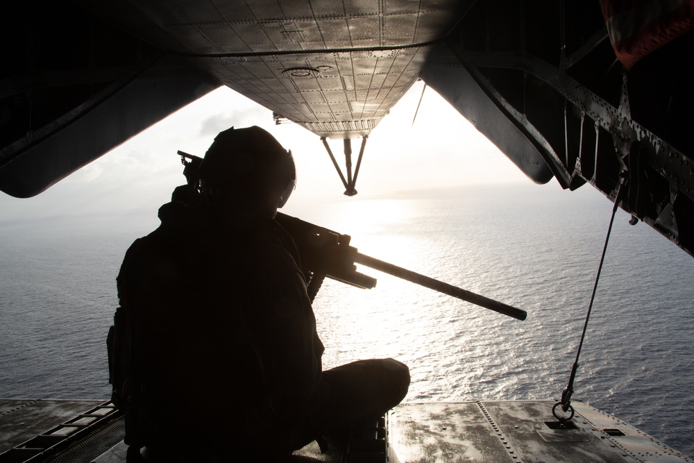 Marine sitting on the rear of a CH-53 during a flight over the ocean