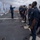 USS MOMSEN Conducts Live Fire Gun Shoot at Sea A firearms qualification or training exercise is taking place on the flight deck of a naval vessel at sea. An instructor in a blue jacket is briefing a line of Navy personnel in dark blue coveralls, with pistols placed on the deck in front of each shooter. Human silhouette paper targets are mounted on a wooden frame to the left side of the improvised shooting range.