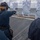 USS MOMSEN Conducts Live Fire Gun Shoot at Sea A female sailor wearing Navy blue coveralls and hearing protection is firing a handgun at silhouette paper targets on the deck of a naval vessel at sea. The training exercise appears to be a qualification or familiarization shoot conducted on the ship's fantail or deck area. Several observers in similar Navy uniforms are watching from behind the shooter.