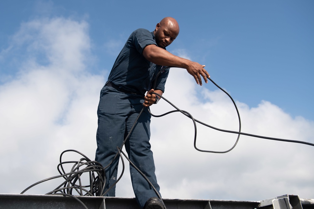 U.S. Navy Airman Apprentice Caleb Sims, from Bromulus, Michigan, untangles the wire from the Union Jack flag pole on the flight deck of the aircraft carrier USS John C. Stennis