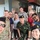 A group selfie photograph showing approximately 11 people, a mix of military personnel in various uniforms and civilians, posing together in what appears to be an outdoor covered area or building. The group includes individuals wearing Thai Royal Army camouflage uniforms with black berets, US Army multicam uniforms, and civilian clothing. The setting and uniform mix suggests a joint military cooperation or exercise event.