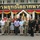 A group of approximately 18 individuals pose for a formal group photograph in front of a Thai military building, identifiable by the Thai script signage reading 'กรมยุทธโยธาทหารบก' (Royal Thai Army Corps of Engineers). The group consists of a mix of U.S. military personnel in camouflage uniforms, Thai military personnel in black uniforms, and civilians in casual attire. Two individuals in the front center appear to be shaking hands, suggesting a formal meeting or diplomatic exchange.