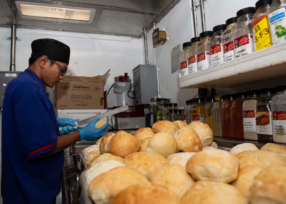 USS Normandy Sailor Cuts Bread Rolls