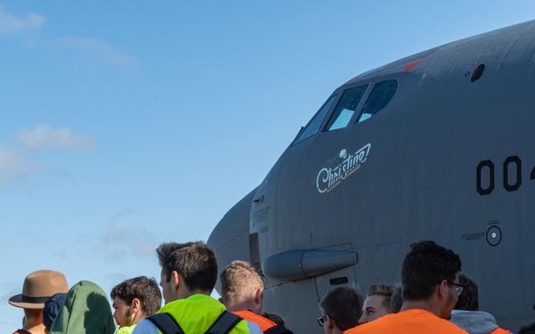 A group of visitors wearing high-visibility safety vests in orange and yellow are gathered on an airfield tarmac, viewing a large gray military transport aircraft up close. The aircraft bears the nose art name 'Christine' and the tail number '0041'. This appears to be an organized airshow or base open day event.