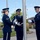 POW/MIA Remembrance Week begins on Peterson Air Force Base Three United States Air Force personnel in dress blue uniforms are performing a flag ceremony at a flagpole, likely a retreat or reveille ceremony. They are wearing white gloves and handling the halyard and flag at the base of a metal flagpole. The setting appears to be an outdoor plaza or courtyard of a military installation.