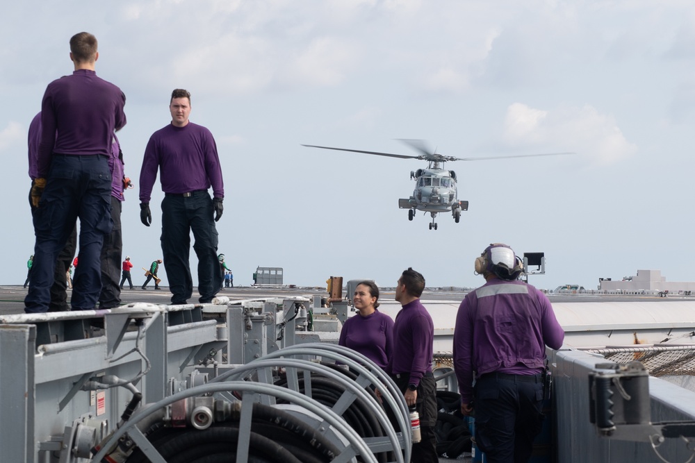 U.S. Sailors watch as a MH-60R Sea Hawk departs from the flight deck of the aircraft carrier USS John C. Stennis (CVN 74)