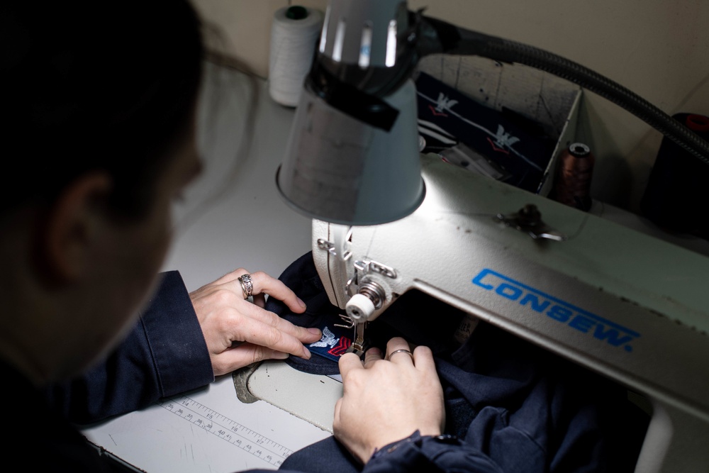 U.S. Sailor sews a rank tab onto coveralls