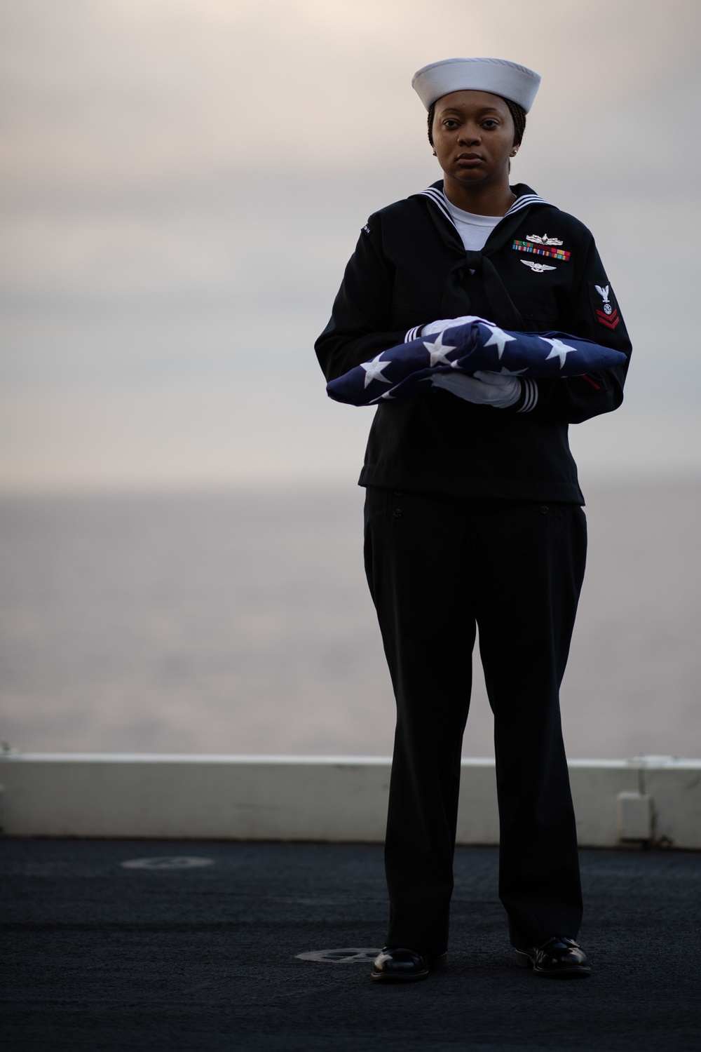 U.S. Navy Religious Programs Specialist 2nd Class Che’lese Bowman, from Clover, Virginia, holds the U.S. flag during a burial at sea