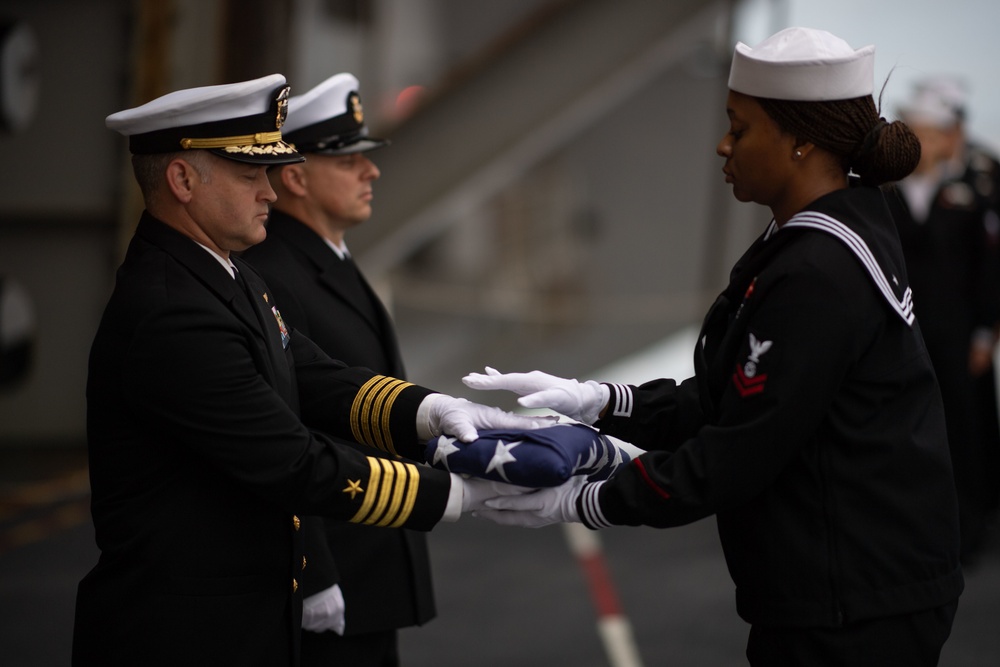 U.S. Navy Religious Programs Specialist 2nd Class Che’lese Bowman, from Clover, Virginia, right, presents Capt. Randy Peck, left, commanding officer of the aircraft carrier USS John C. Stennis (CVN 74), with an American flag during a burial at sea