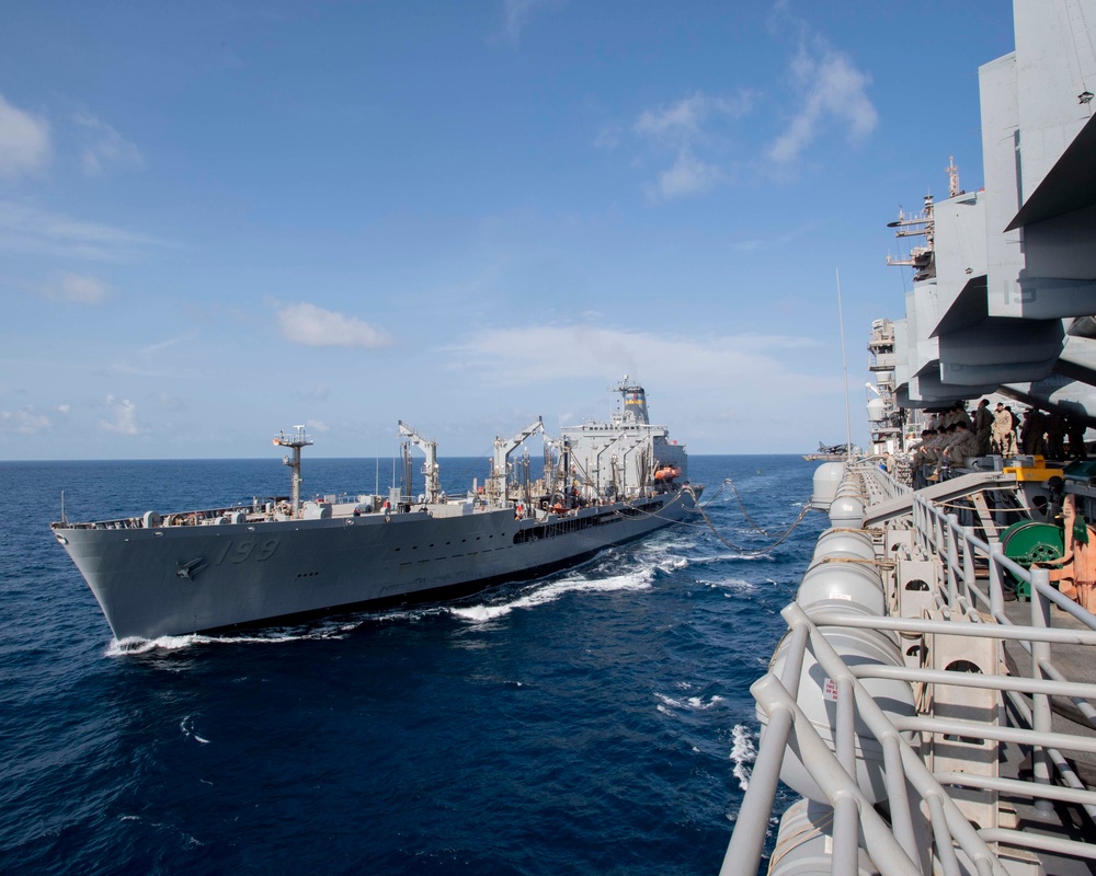 Two naval vessels are conducting an underway replenishment (UNREP) operation at sea. The ship on the left, bearing hull number 199, appears to be a replenishment oiler or supply vessel transferring fuel or supplies to the larger vessel on the right. Personnel are visible on the deck of the right-side vessel observing the operation.
