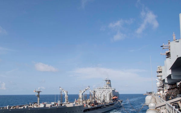 Two naval vessels are conducting an underway replenishment (UNREP) operation at sea. The ship on the left, bearing hull number 199, appears to be a replenishment oiler or supply vessel transferring fuel or supplies to the larger vessel on the right. Personnel are visible on the deck of the right-side vessel observing the operation.