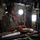 Saving Lives in the Battlespace A female military aviator in an olive green flight suit is working at a workstation inside a military aircraft. She is wearing aviation headphones and reviewing documents or a checklist on a clipboard. The interior setting, circular porthole window, and equipment visible suggest this is the cargo or crew area of a large military transport aircraft.