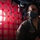 Saving Lives in the Battlespace A military personnel member wearing Air National Guard flight gear, including an oxygen mask and helmet-mounted equipment, is photographed inside what appears to be a military aircraft. The interior is illuminated by red lighting, with a cargo net or restraint webbing visible against a porthole window. The image has a dramatic, high-contrast aesthetic typical of military operational photography.