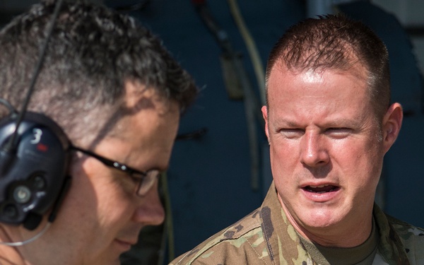 Two individuals are engaged in a conversation in what appears to be a military aviation environment. The person on the right is a U.S. Air Force service member in OCP (Operational Camouflage Pattern) uniform with the name tape 'HOFFMAN' and a Chief Master Sergeant rank insignia visible. The person on the left is wearing a headset and civilian-style clothing, appearing to be a ground crew member or technician.