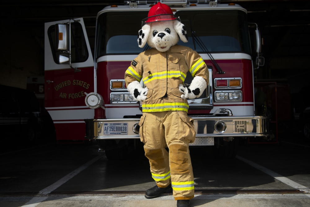 Sparky stands in front of a fire truck.