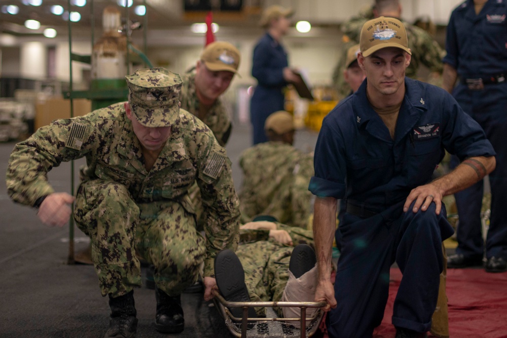 U.S. Sailors lift a simulated patient in a stretcher during a mass casualty drill in the hangar bay