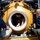 Three individuals are working around the circular hatch of a large yellow submersible or hyperbaric vessel. One person is positioned inside the hatch opening, appearing to work on the sealing mechanism, while two others assist from outside. The setting appears to be on a ship deck or platform under bright daylight conditions.