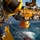 A worker on an offshore platform is guiding a large yellow remotely operated vehicle (ROV) or subsea equipment module during a deployment or recovery operation over open ocean. The heavy industrial machinery, painted predominantly yellow, is suspended over the water from a crane or A-frame structure. The scene depicts an active offshore oil and gas or subsea operations environment.