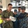 A U.S. Navy sailor identified by name tape as 'BABICK' is reviewing documents with personnel wearing Vietnamese People's Navy uniforms aboard what appears to be a naval vessel's bridge or command area. The interaction suggests a multinational military exchange, training exercise, or ship tour. Additional personnel in the background include individuals in civilian attire and what appears to be an Australian military uniform.