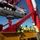 A deep-sea rescue or research submersible is being deployed or recovered using a large red A-frame crane structure aboard a vessel at sea. Several crew members in high-visibility safety gear and hard hats are overseeing the operation on the deck. One individual appears to be wearing a naval uniform, suggesting a military or government-affiliated operation.