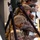 Multiple military personnel in desert MARPAT camouflage uniforms and combat helmets are positioned along a staircase railing, appearing to observe or surveil an area below. The foreground soldier is using a handheld optical device, possibly a laser rangefinder or spotting scope, while others lean over the railing in observation postures. The scene suggests a tactical training exercise or operational surveillance activity.