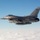 A U.S. Air Force F-16 Fighting Falcon jet fighter is photographed in flight above a cloud layer against a clear blue sky. The aircraft bears tail markings 'ET' and '96 TW', identifying it as belonging to the 96th Test Wing based at Eglin Air Force Base, Florida. The aircraft is carrying external ordnance and stores on its hardpoints.