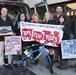 A group of seven adults pose in front of a van loaded with toys for the Marine Corps Reserve Toys for Tots charity drive. They are holding various donated toys including a bicycle, an LOL Surprise set, a toy police truck, and a Frozen II art set. The banner they display identifies this as a Marine Corps Reserve Toys for Tots donation event.