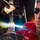USS Wayne E. Meyer (DDG 108) Hull Technician Braising A young male worker wearing dark safety glasses and a red shirt with 'ADAMS' text is performing a torch brazing or soldering operation on a metal pipe or fitting. A bright blue-white flame is visible emanating from a torch nozzle held by a vise grip, with the worker feeding filler rod into the joint. The image is a close-up shot taken in what appears to be an industrial or workshop environment.