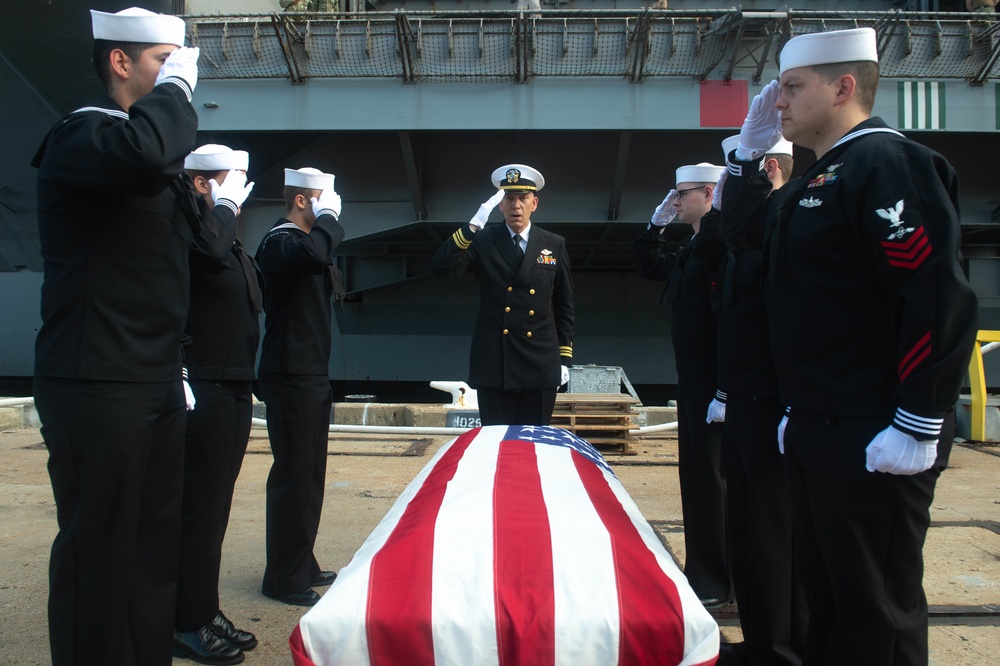 U.S. Sailors salute a service member’s remains on the pier