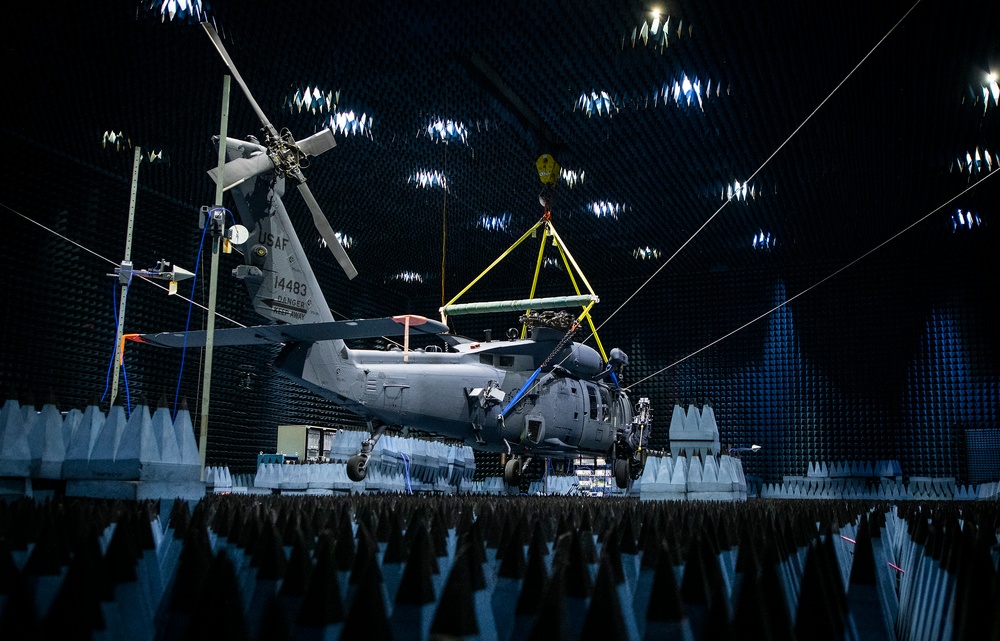A USAF military helicopter, bearing tail number 14483, is positioned inside a large anechoic chamber lined with pyramid-shaped RF/acoustic absorber foam on all walls and ceiling. The helicopter appears to be undergoing electromagnetic compatibility (EMC) or radar cross-section testing, suspended or stabilized with yellow lifting rigging and cables. The controlled testing environment is designed to eliminate external electromagnetic interference or sound reflections.
