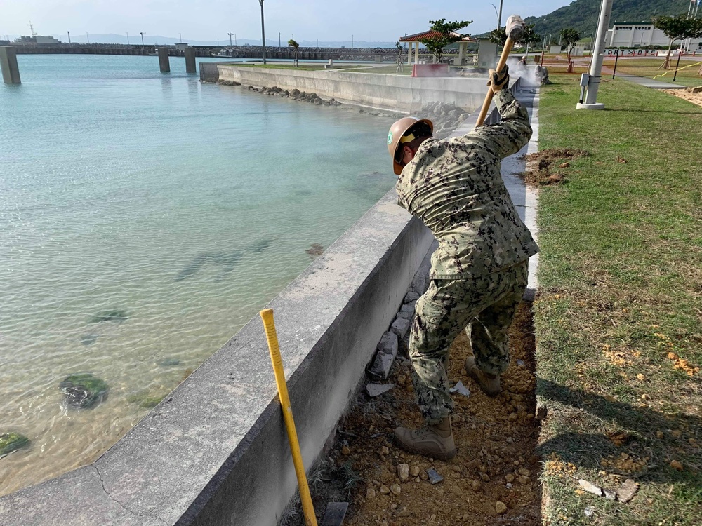 U.S. Navy Seabees replace sidewalks and repair a seawall on board Naval Base White Beach